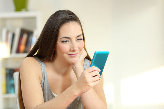 Smiley girl reading messages in a smart phone at home