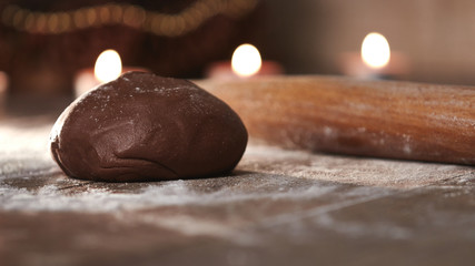 Ginger dough for gingerbread on a wooden table. Scattered flour and candles in the background. Preparing for baking gingerbread for Christmas.