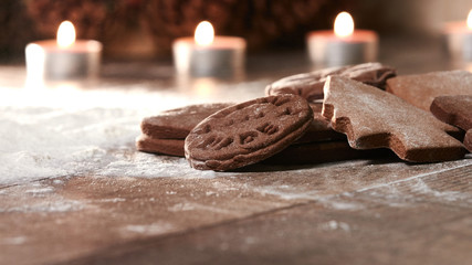 Gingerbread cookies on a wooden table. Scattered flour and candles in the background. Baking gingerbread for christmas.