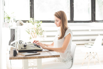 Young business woman working at home and typing on a typewriter. Creative Scandinavian style workspace