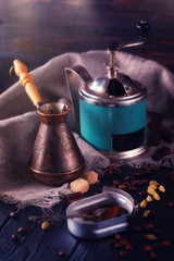 Close-up shot of vintage hand-operated old coffee grinder, roasted beans, chocolate, badyan, cardamom and cezve on a rustic wooden table.