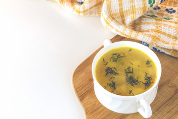 Chicken soup with dill in a white bowl on a wooden cutting board and yellow kitchen towel. Healthy soup with copy space.