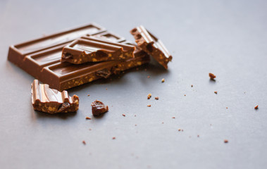 Chunks of milk chocolate with crushed hazelnuts and raisins with alcohol on black background. Confectionery degustation.