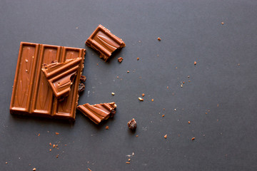 Confectionery degustation. Pieces of milk chocolate with crushed hazelnuts and raisins with alcohol on black background.