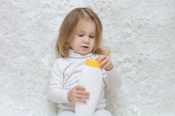 Cute little girl keeping white plastic shampoo bottle in her hands, looking at the camera. Baby...