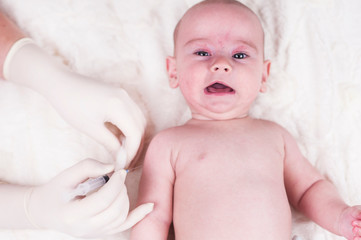 A very small child, a baby, is lying in the doctor's office and the doctor makes an injection.