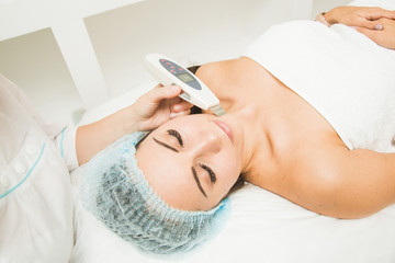 Beautician does the procedure of ultrasonic face cleaning for a young woman in a beauty salon