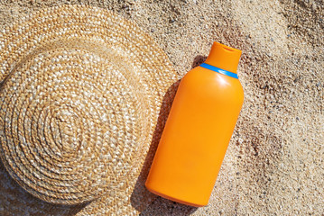 Do not forget to protect yourself during summer vacations. Sunscreen protection cream and sun hat are  laying on the sand at the beach.