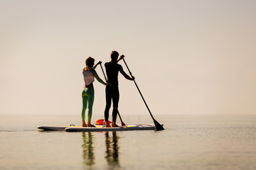 Young couple doing sup yoga on sunset background