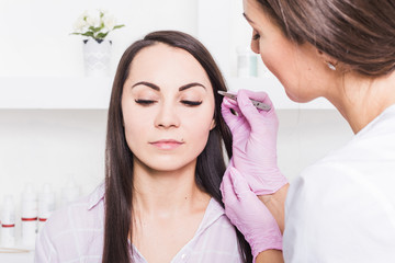 Beautician plucks a young woman's eyebrows with tweezers