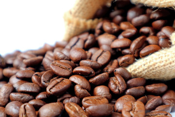 Closed up roasted coffee beans scattered from burlap sack on white background  