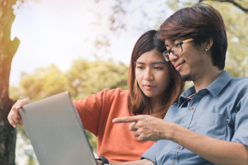 Young asian man and woman working with them laptop on a bench in the park outdoors on vacation time.