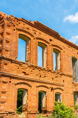 A large ruined ancient house of red brick against a blue sky with white clouds.