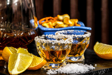 Tequila shots with salt, lemon and snacks. Mexican gold tequila in short glasses on wooden table.