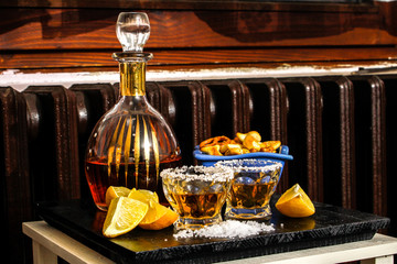 Tequila shots with salt, lemon and snacks. Mexican gold tequila in short glasses on wooden table.