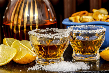 Tequila shots with salt, lemon and snacks. Mexican gold tequila in short glasses on wooden table.