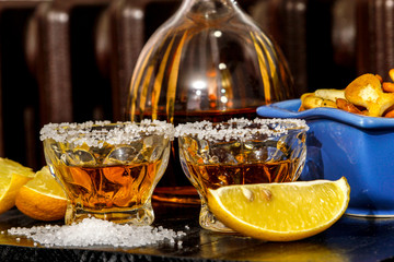 Tequila shots with salt, lemon and snacks. Mexican gold tequila in short glasses on wooden table.