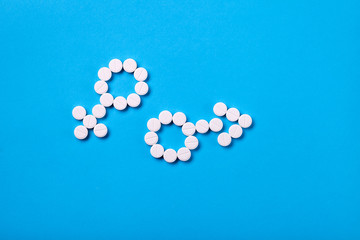 Gender symbols of male and female origin from white round pills on blue background with copy space place for text. Top view.