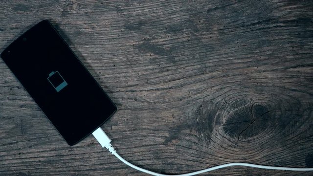 smart phone charging connected with white cable on grunge wood background