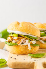 Grilled chicken and avocado burger on wooden board.