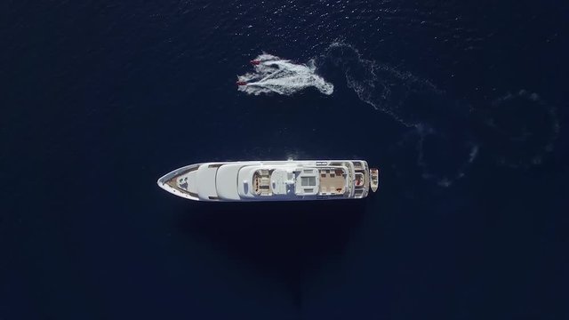 Aerial view of two jet-ski draw a half circle round the private huge yacht