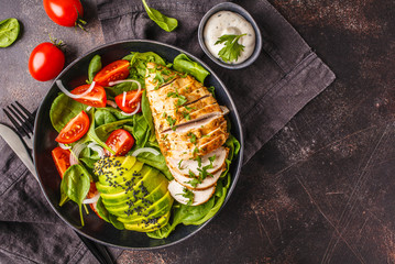 Grillwd chicken breast and avocado salad with spinach, tomatoes and Caesar dressing, dark background, top view. - obrazy, fototapety, plakaty