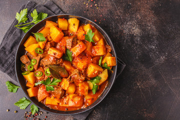Spicy beef stewed with potatoes in tomato sauce in black plate. Meat traditional goulash.