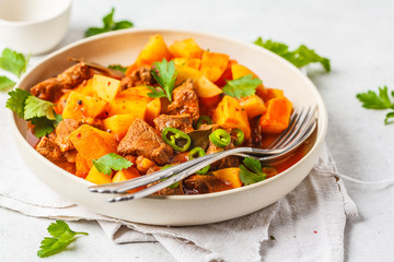 Spicy beef stewed with potatoes in tomato sauce in white plate. Meat traditional goulash.