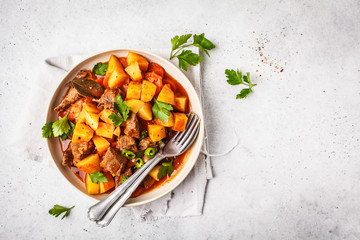 Spicy beef stewed with potatoes in tomato sauce in white plate, top view.