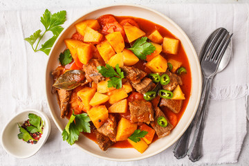 Spicy beef stewed with potatoes in tomato sauce in white plate, top view.