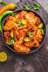 Spicy grilled chicken wings in tomato sauce in a black plate on a dark background.