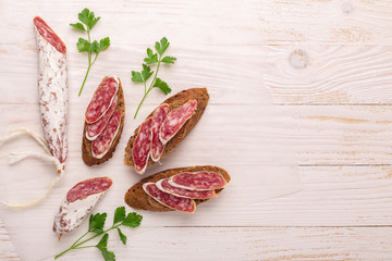 Salami and bread on white wooden background. Top view.