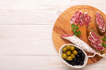 Salami and bread on white wooden background. Top view.