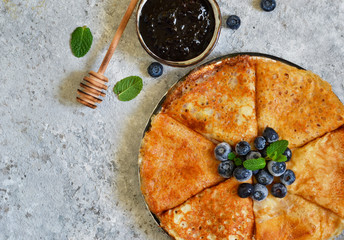 Thin pancakes with blueberry jam on a concrete background with poxt space.