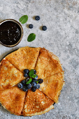 Thin pancakes with blueberry jam on a concrete background with poxt space.
