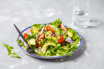 Healthy arugula, avocado, tomatoes salad on gray background, top view.