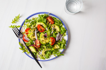 Healthy arugula, avocado, tomatoes salad on white marble background.