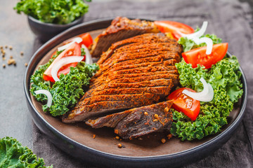 Spicy baked beef with kale salad in black plate on dark background.