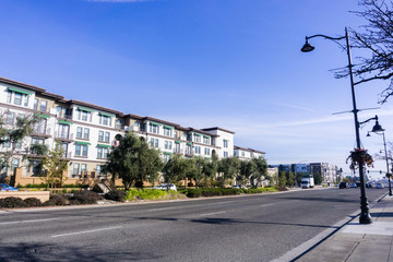 Fototapeta na wymiar Light traffic on a street in Santa Clara on a sunny day, multifamily housing development on the side of the road; San Francisco bay area, California