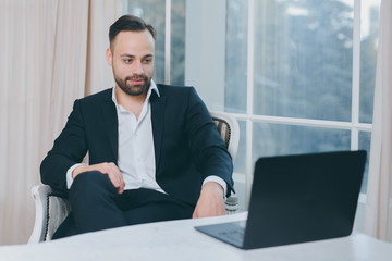 Fototapeta premium Hipster bearded businessman in suit with laptop on window background