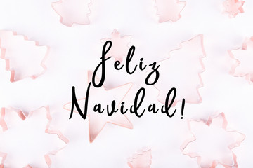 Flatlay with selection of holiday copper cookie cutters on white sparkling background. Holiday, Christmas card concept. Cozy homey details. Holiday wording in Spanish