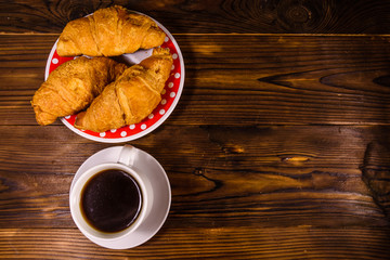 Cup of dark coffee and croissants on wooden table. Top view