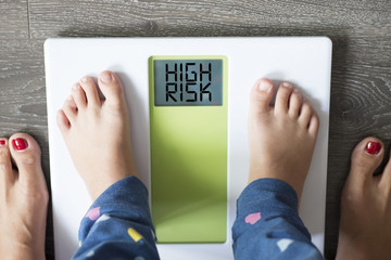 Childhood obesity high risk for health problems with child’s feet on weight scale  under the supervision of his mother  - obrazy, fototapety, plakaty