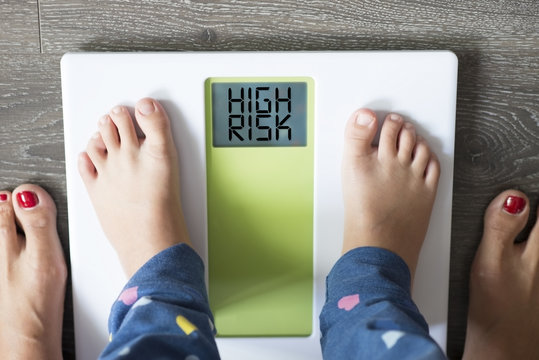 Childhood obesity high risk for health problems with child’s feet on weight scale  under the supervision of his mother 