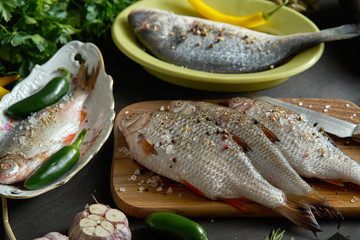 a set of several fresh, raw fish in various dishes and with vegetables on a black table