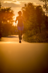 Fototapeta na wymiar Young woman running outdoors on a lovely sunny summer evening (shallow DOF; color toned image)