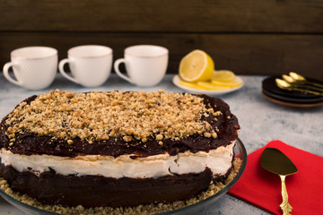 Chocolate dessert with walnuts. Layer of white cream. Utensils for tea. Wooden background.