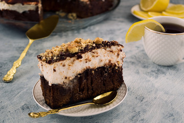 Piece of chocolate cake. Layer of white cream. Sprinkled with walnuts. Cup of tea and lemon. Dishes for dessert.