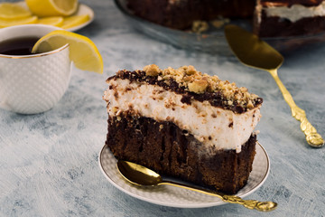 A sliced piece of chocolate cake. Brown and white layer. Crushed walnut. White Cup of tea. Slice of lemon.