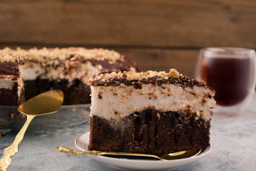 Piece of chocolate cake on a plate. White and brown layer. Crushed walnut. Spoon and spatula for dessert. Wooden background.